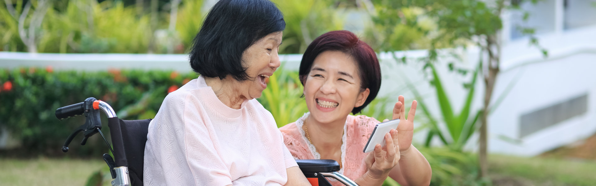 Senior woman in a wheel chair together with her caregiver are watching funny videos