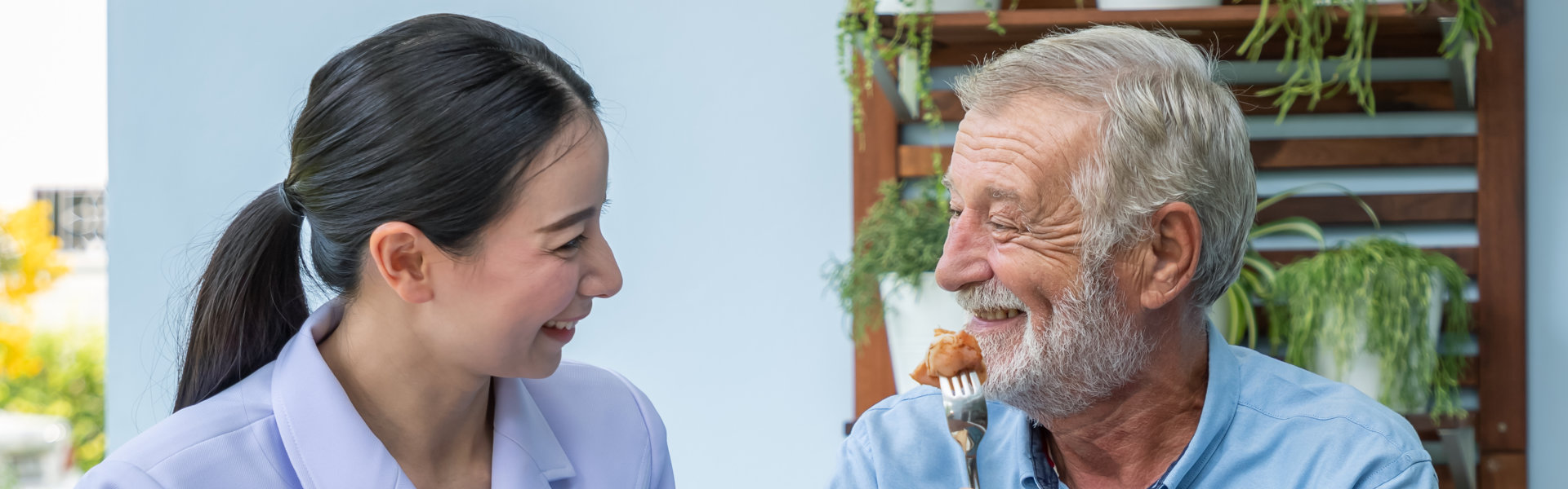 Female caregiver taking care the elder man while feeding him