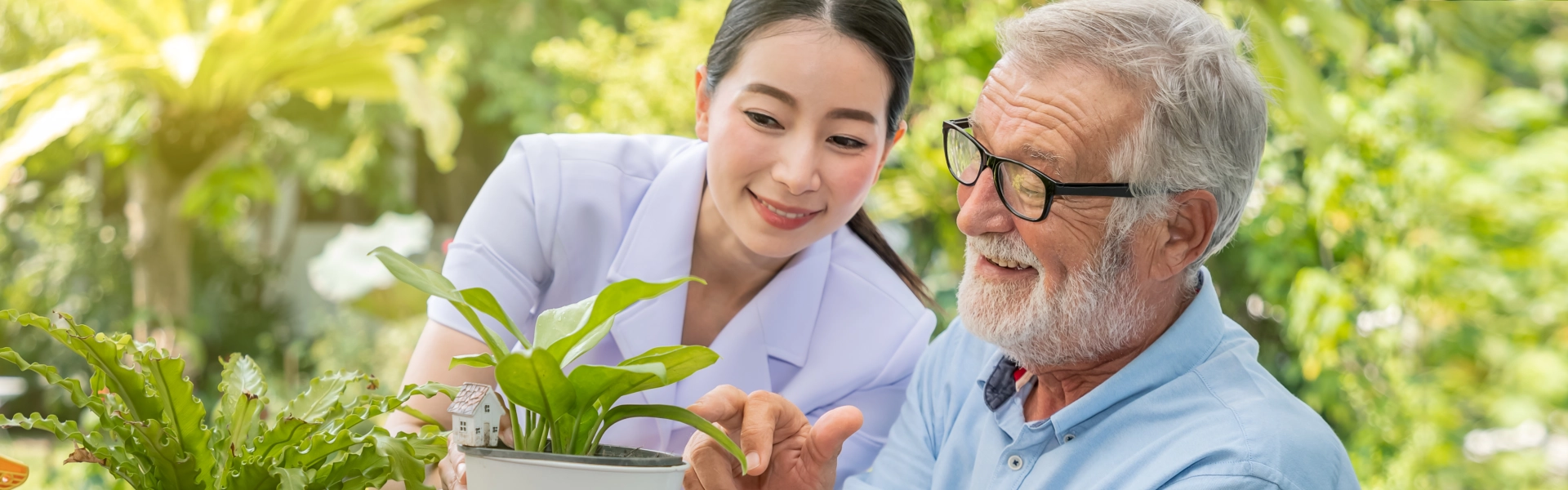 female caregiver with elderly man smiling looking at a plant