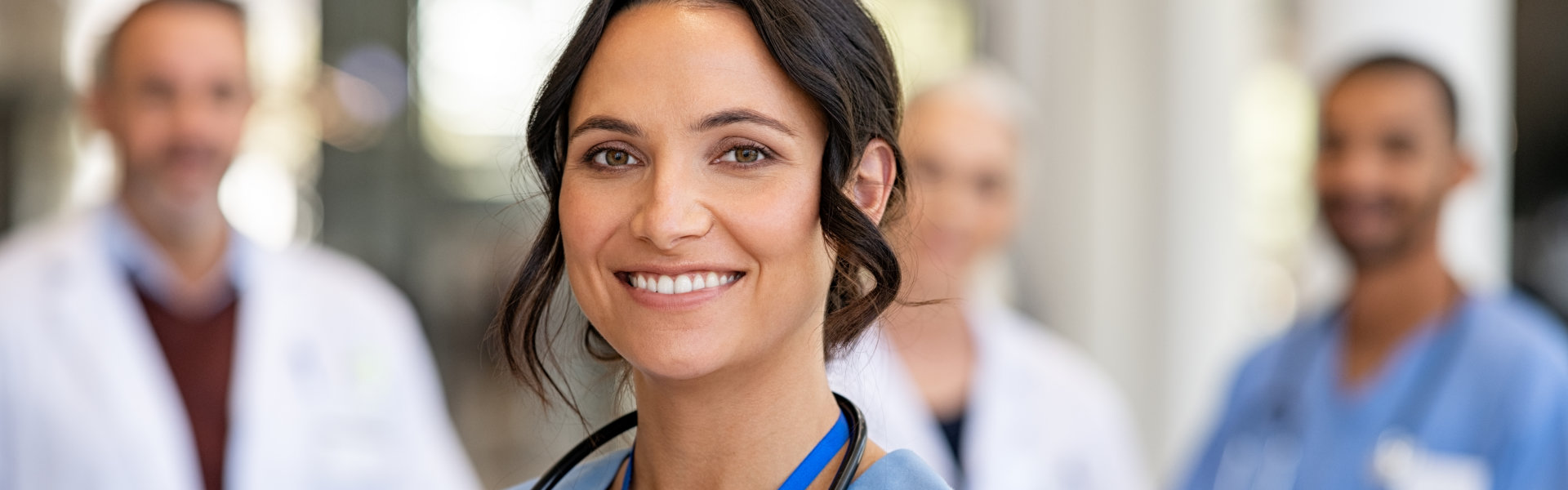 Portrait of happy young nurse in uniform with healthcare team in background.